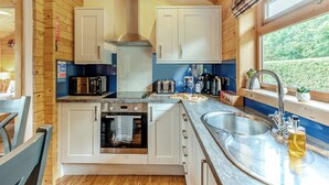 A modern kitchen with wooden walls, white cabinets, a stainless steel sink, and a window with a view of greenery. - 2 bedroom accommodation in Ellesmere (Ellesmere)
