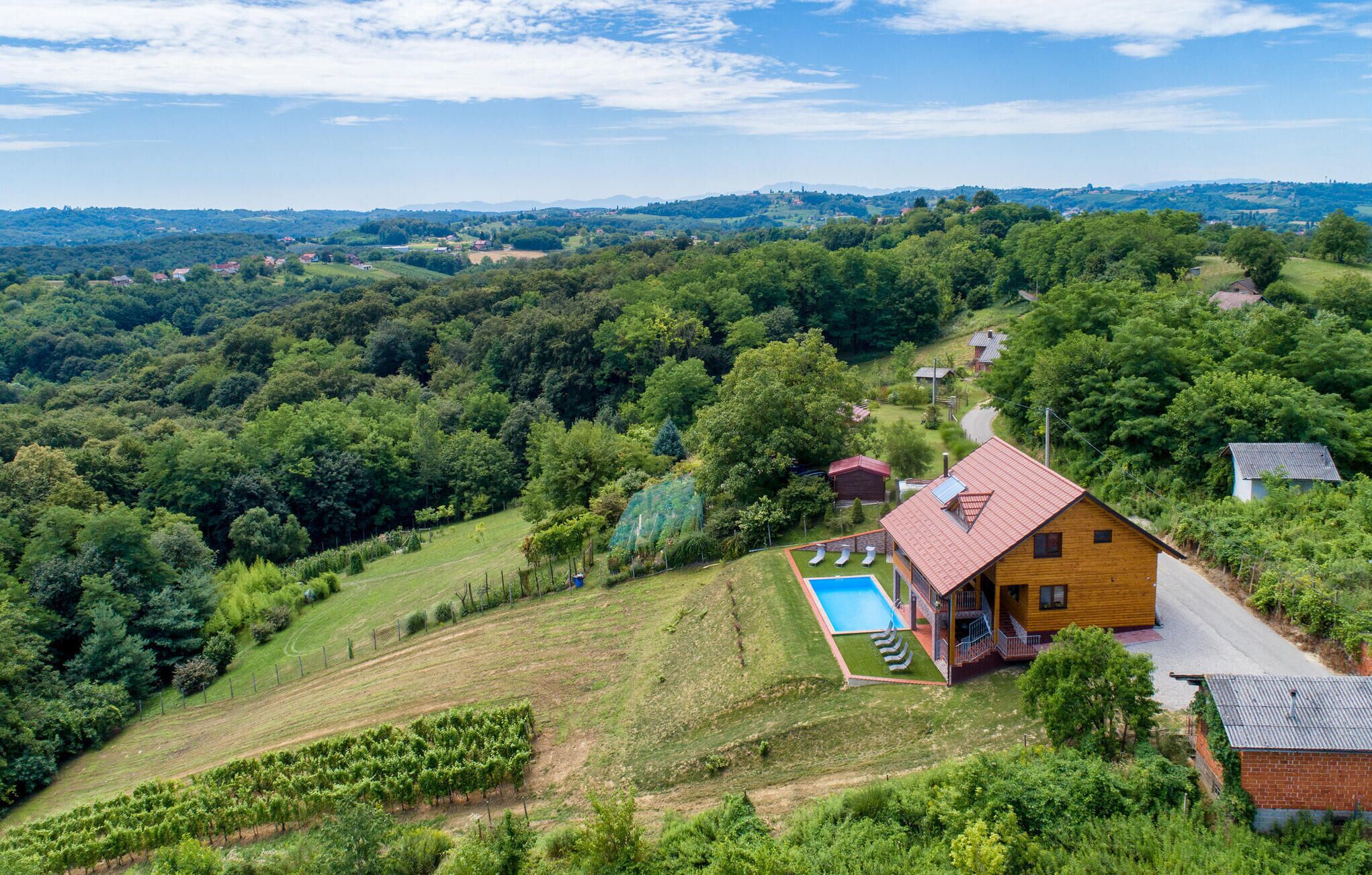 Ein Holzhaus mit rotem Dach, einem Swimmingpool und einem Weinberg.