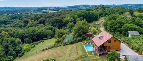 Ein Holzhaus mit rotem Dach, einem Swimmingpool und einem Weinberg.