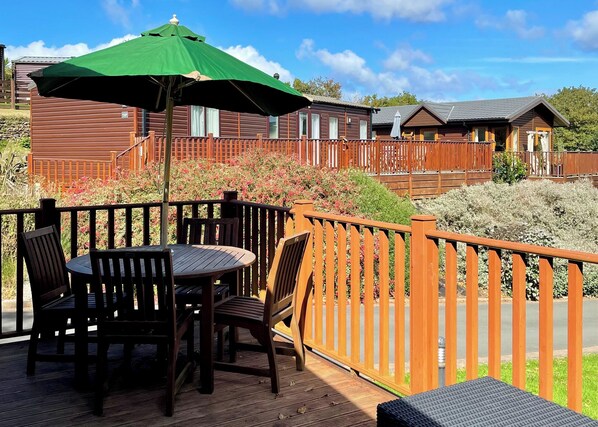 A wooden deck with a table and chairs, surrounded by a wooden fence, and a green umbrella.