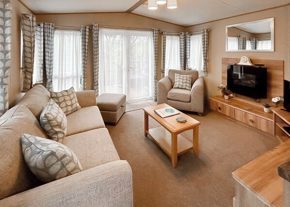 A living room with a sofa, armchairs, a coffee table, a television, and a mirror. - Country Holiday Home Platinum Four Spa (Tintagel)