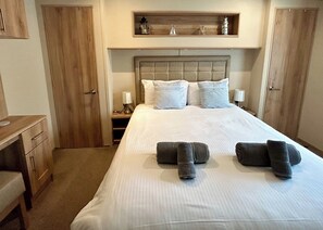 Una cama bien hecha con almohadas, una mesita de noche con lámpara y un cabecero de madera.