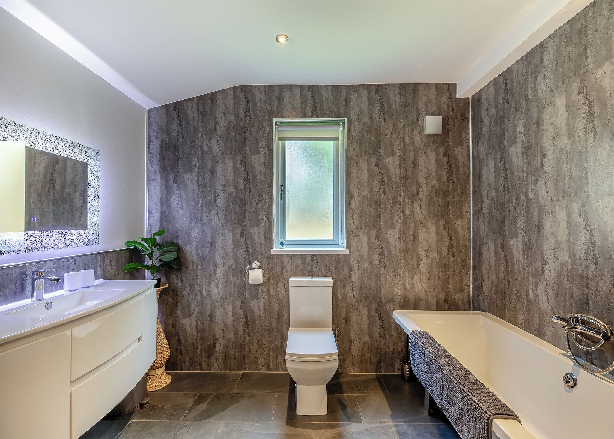 Un baño moderno con inodoro blanco, bañera blanca y un amplio ventanal.