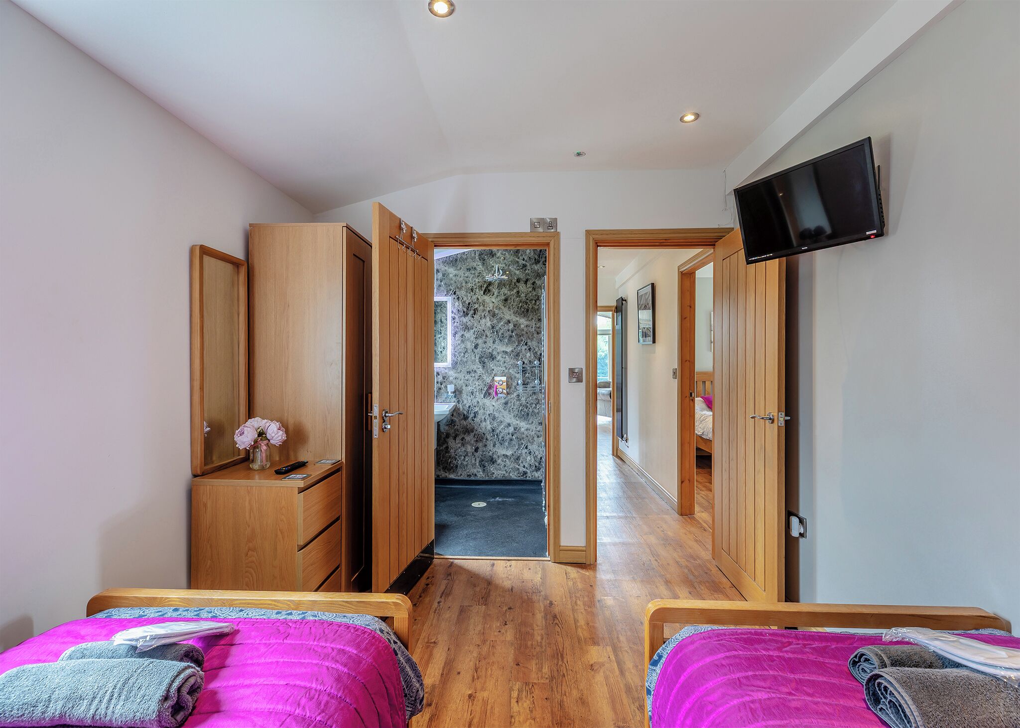 A bedroom with two beds, wooden wardrobe, a TV, and a bathroom visible through an open door.