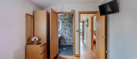 A bedroom with two beds, wooden wardrobe, a TV, and a bathroom visible through an open door.