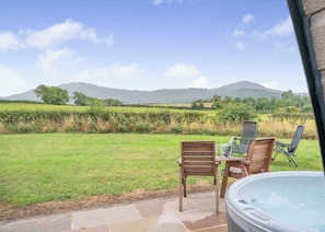 A patio with a hot tub, wooden chairs, and a table with a laptop.