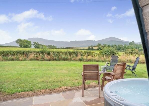 A patio with a hot tub, wooden chairs, and a table with a laptop.