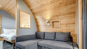 Un interno moderno con soffitto curvo, un divano modulare grigio, un letto con lenzuola bianche e pareti rivestite in legno.