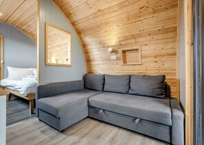 A modern interior with a curved ceiling, a grey sectional sofa, a bed with white linens, and wooden panel walls. - 0 bedroom accommodation in Great Busby (Great Busby)