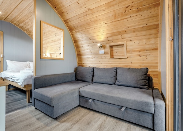 A modern interior with a curved ceiling, a grey sectional sofa, a bed with white linens, and wooden panel walls.