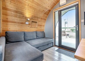 A modern interior with a wooden ceiling, a grey sectional sofa, and a sliding glass door leading outside.
