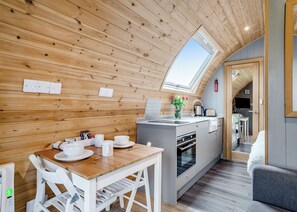 A compact kitchen with wooden walls, a skylight, and a small dining area with white furniture.