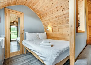 A bedroom with a curved ceiling, a bed with white linens, a wooden wall, and a door leading to an outdoor area.