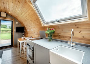 A modern kitchen with wooden walls, a large window, a built-in TV, and a sink.