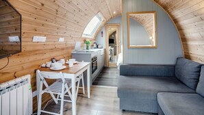 Un ambiente accogliente e compatto con soffitto in legno, zona pranzo con tavolo e sedie, un divano grigio e una cucina visibile attraverso un arco.