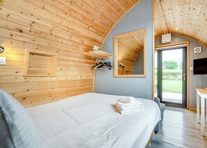 A wooden-paneled room with a bed, a mirror, a TV, and a door leading outside.