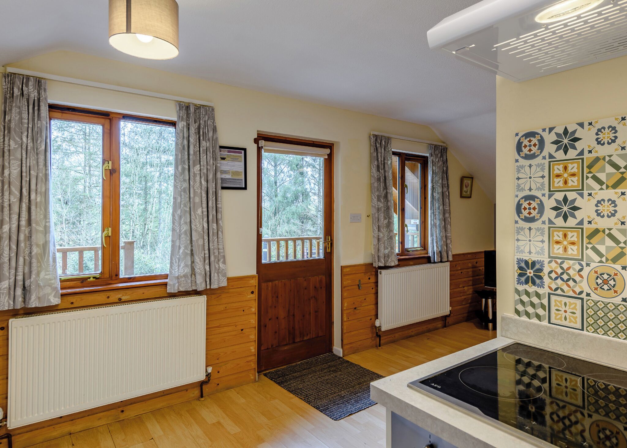 A room with wooden walls, a radiator, a window with curtains, a door, and a tiled backsplash.