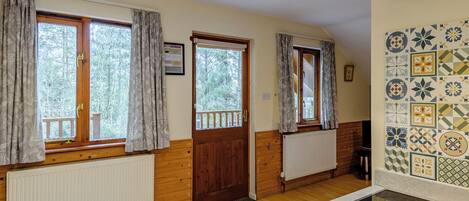 A room with wooden walls, a radiator, a window with curtains, a door, and a tiled backsplash.