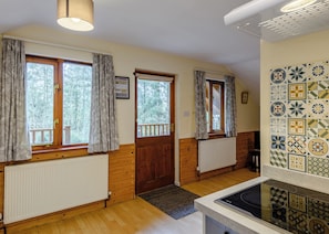 Ein Zimmer mit Holzwänden, einem Heizkörper, einem Fenster mit Vorhängen, einer Tür und einer gefliesten Rückwand.