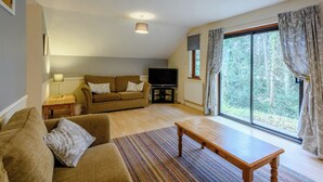 A living room with a sofa, a coffee table, a television, and a large window with curtains.