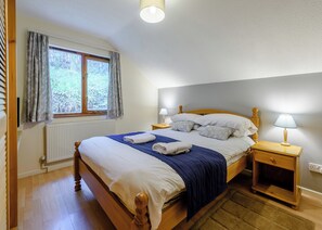 Un dormitorio con una cama de madera, dos mesitas de noche, una ventana con cortinas, un radiador y una lámpara en el techo.