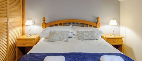 A neatly made bed with a blue bedspread, two white towels, and two bedside lamps.