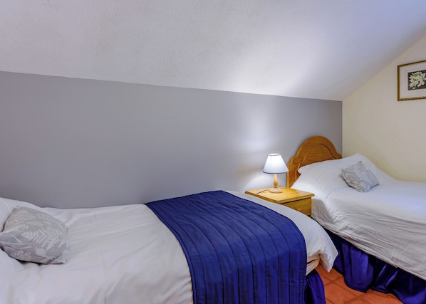 Hotellihuone, jossa on kaksi sänkyä, yöpöytä lampun kanssa ja seinällä oleva kehystetty kuva.