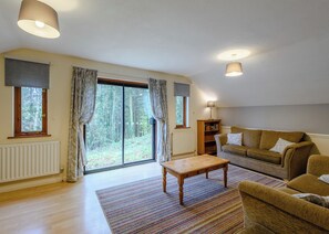 A living room with a sofa, a coffee table, a lamp, and a bookshelf. - Timber lodge set in an elevated woodland position with views of the lake. (Webbery, Bideford)