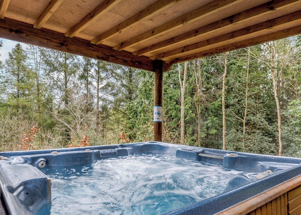 Ein Whirlpool unter einer Holzpergola mit Blick auf einen Wald.
