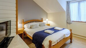 A bedroom with a wooden bed, bedside lamps, a TV, and a window with curtains.