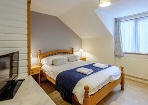 A bedroom with a wooden bed, bedside lamps, a TV, and a window with curtains. - Timber lodge set in an elevated woodland position with views of the lake. (Webbery, Bideford)
