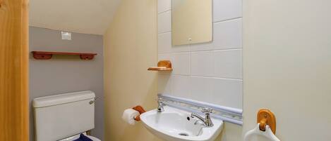 A bathroom with a toilet, sink, mirror, towel rack, and wooden shelf.