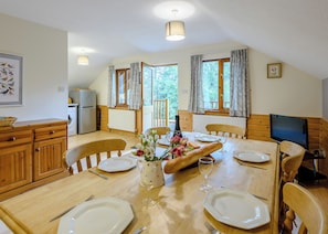 A dining area with a wooden table set for four, a bouquet of flowers, and a television on the right. - Timber lodge set in an elevated woodland position with views of the lake. (Webbery, Bideford)