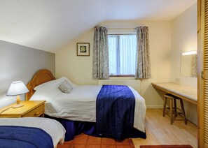A bedroom with a bed, bedside table, lamp, window with curtains, and a desk with a chair.