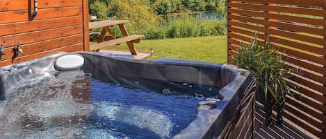 A hot tub with a wooden deck, a wooden fence, and a picnic table.