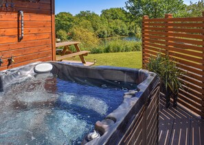 A hot tub with a wooden deck, a wooden fence, and a picnic table. - Perfectly positioned with panoramic views of the lake. (Anglesey)