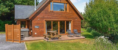 A wooden cabin with a patio, a hot tub, and a covered outdoor seating area.