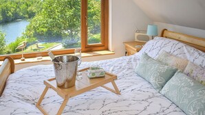 Une chambre à coucher avec un lit, une table de chevet avec une lampe, une radio et une vue sur une rivière et des arbres.