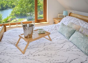 Un dormitorio con una cama, una mesita de noche con lámpara, una radio y vistas a un río y árboles.