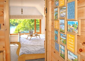 A wooden room with a bed, a small table with a basket, and a window with a view of greenery. - Perfectly positioned with panoramic views of the lake. (Anglesey)