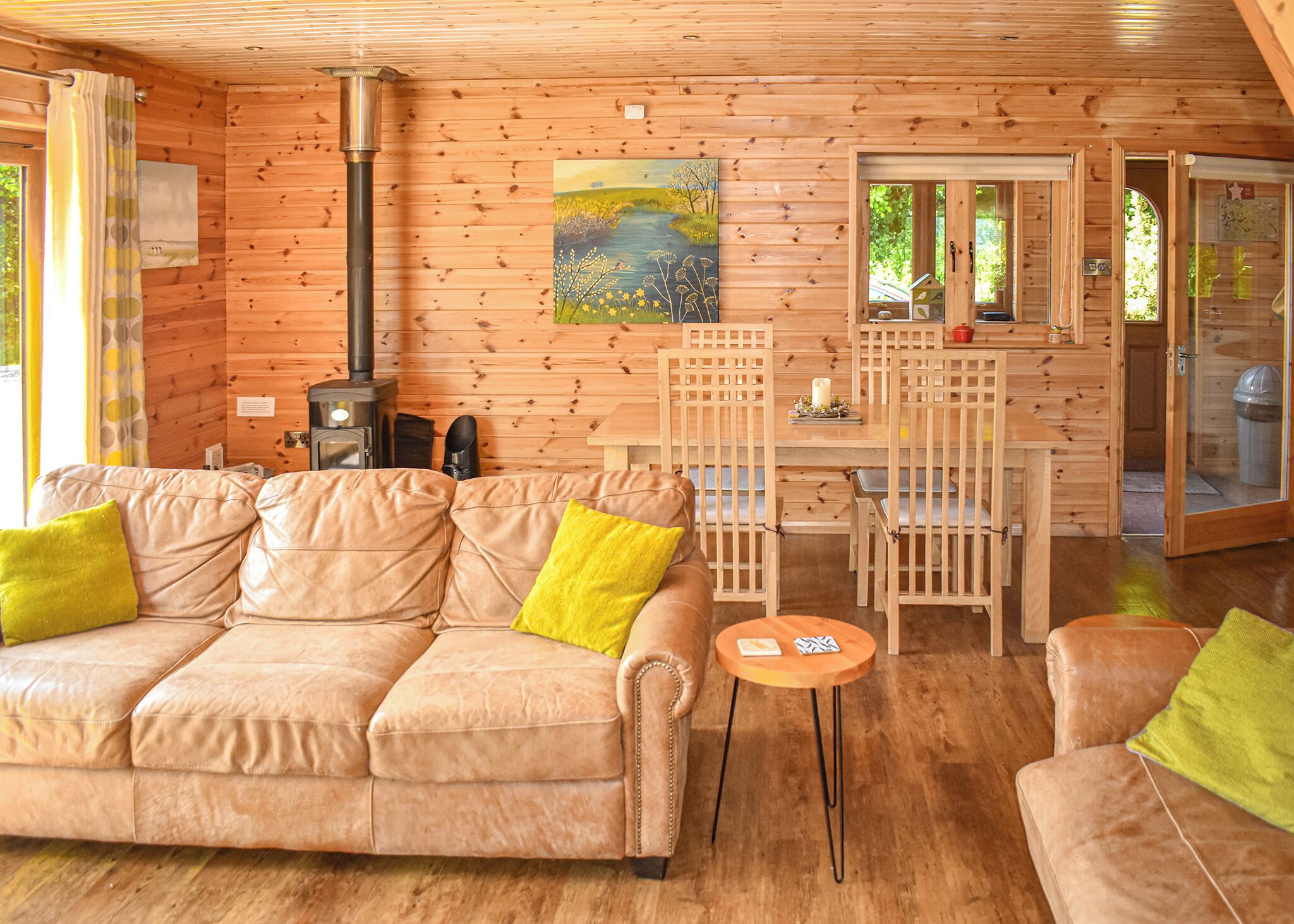 A cozy cabin interior with a leather sofa, wooden dining table, and a painting on the wall.