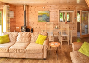 A cozy cabin interior with a leather sofa, wooden dining table, and a painting on the wall. - Perfectly positioned with panoramic views of the lake. (Anglesey)