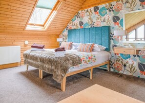 Une chambre confortable avec un plafond en pente, un lit en bois, une tête de lit bleue et un papier peint à motifs floraux.