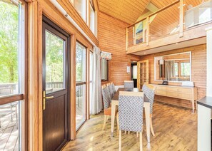 A wooden cabin interior with a dining area, a kitchen, and a balcony.