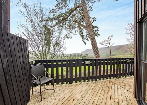 A wooden deck with a bench, a black fence, and a view of a rural landscape with hills.