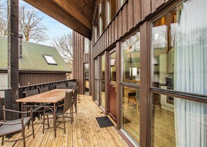 A wooden deck with a table and chairs, large windows, and a view of the house interior. - 3 bedroom accommodation in Millom (Millom)