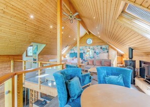 A wooden interior with a balcony, a sofa set, a television, and a fireplace.