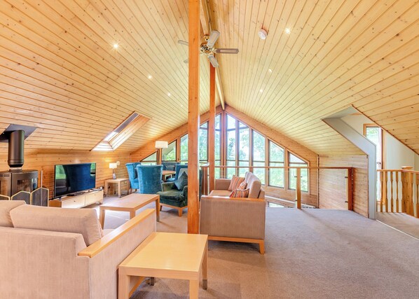 A cozy loft-style room with a high ceiling, wooden beams, a fireplace, a TV, and comfortable seating.