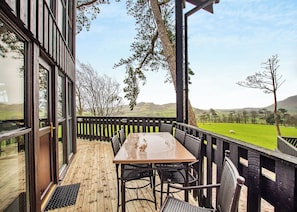 A wooden deck with a table and chairs, overlooking a green field with sheep.