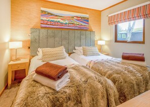 A hotel room with two beds, a wooden headboard, patterned curtains, and a painting above the beds.